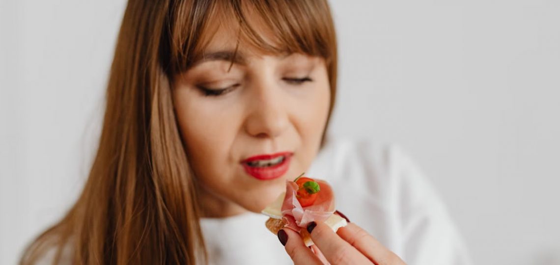 Woman with long hair savoring a gourmet canape indoors.